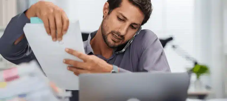 Man on telephone holding papers with laptop in front